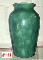 Front view of large green glazed pottery vase against a white brick wall.