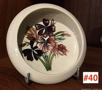 Front view of Moorcroft small bowl/dish showing floral design inside with purple, pink, orange flowers and green stems on cream background.