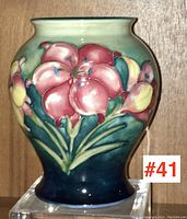 Front view of glazed ceramic Moorcroft vase showing pink and yellow flowers with green leaves on blue to green gradient background.
