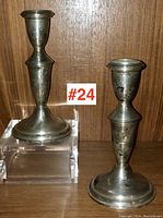 Pair of tarnished sterling silver Birks candlesticks on a wooden shelf, one elevated on a clear acrylic block.
