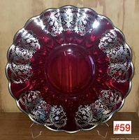 Full front view of ruby glass charger plate displaying the sterling silver floral and urn overlay pattern around scalloped rim.