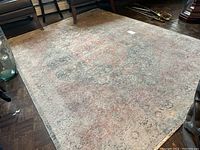 Full view of rosewood color area rug on hardwood floor surrounded by chairs, showing overall faded floral pattern and signs of wear.