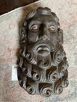 Front view of a dark wooden carved face mask showing detailed curly hair, beard, expressive eyes with painted highlights.