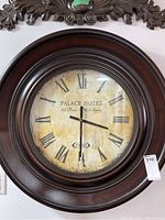 Full view of large round wall clock with dark wooden frame, roman numeral clock face, and Palace Hotel Paris text on the dial.