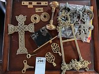 Full view of various brass items including Celtic cross, door knobs, keys, handles, and lock parts on wooden surface