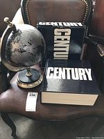 Photo of the Century book with slipcover box and the decorative globe placed on a leather chair.