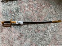 Full view of decorative sword in black sheath with brass accents lying on patterned carpet.