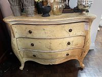 Front view of distressed cream bow front dresser with three drawers and metal knob pulls