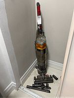 Full upright vacuum with orange cyclone dust bin and red handle, with multiple hose and brush attachments on floor