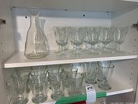 Shelf with clear glass carafe and six stemmed glasses all featuring fleur de lis etching