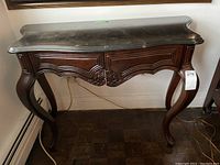 Front angle showing full hall table with dark wood, curved legs, carved drawer fronts, and black faux marble top.