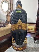 Front view of large carved wooden bust with visible dimensions sticker, showing intricate black, gold, and reddish-brown painted details