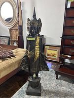 Full view of the tall Indonesian style dark wooden statue with gold accents standing on square base.