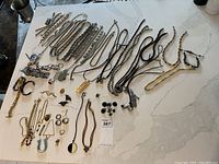 Overview of multiple necklaces, bracelets, rings, pins arranged on a tabletop, showing mixed metals, chain styles, and leather cord necklaces with pendants.