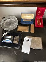 Overview photo displaying all included lighters, cigarette cases, and the ashtray arranged on a surface under a framed mirror.