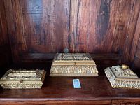 Photo showing all three ornate gold-colored Bombay Co. desk/stamp boxes side by side on a wooden surface