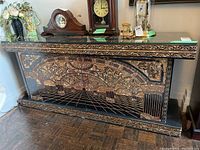 Front view of ornate sideboard with classical Roman/Greek style gold and black design, showing top with clocks and decorative items.