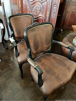 Pair of captain's chairs showing brown leather textured seats and backs, brass stud trim, and black carved wooden frames.