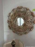 Front view of one mirror showing round reflective glass with elaborately carved wooden frame in distressed white and brown finish with floral and scroll motifs.