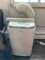 Portable air conditioner unit with attached exhaust hose and accessories on top