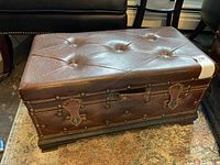Front and side view of brown tufted leather trunk with stud decorations and leather straps, showing aged wear.