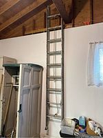 Full view of aluminum extension ladder leaning against the wall near other storage items.
