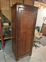 Full view of the antique wooden wardrobe cabinet showing exterior panel door and ornate carved base and legs.