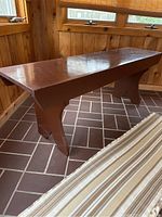 Photo showing wooden bench by a window with no cushion, revealing flat wooden top and brown painted finish.