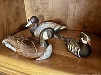 Wide view of three duck figurines on a wooden shelf: two wooden hand carved, one ceramic.