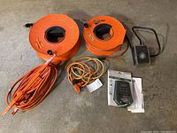 Two large orange extension cord reels, one smaller orange cable reel, an orange multi-outlet extension cord visible on concrete floor.