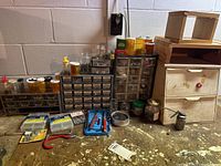 Overview of workbench with small parts drawers filled with assorted fasteners and small hardware, pill bottles with screws inside, and some small wood storage units.