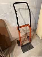 Front perspective of handcart showing orange metal frame, black handle, and black platform base.