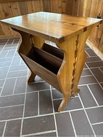 Side view of the wooden side table showing curved legs and built-in magazine rack with arrow inlay design on side panel.