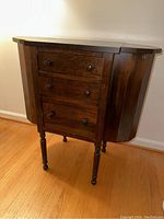Overall view of the dark wood Martha Washington sewing cabinet showing front with three drawers and one side compartment closed.