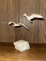 Front view of two cream-colored abstract seagulls mounted on metal rods attached to a white quartz stone base