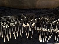 Full overview of all pieces laid out showing knives, forks, soup spoons, teaspoons, dessert forks, and grapefruit spoons in three groups on black fabric.