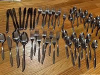 Full collection of flatware including knives, forks, spoons, teaspoons and serving utensils arranged on a wooden surface.