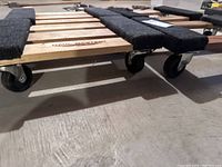 Close-up side angle showing wooden slats with black padding and caster wheels on the dolly.