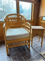 Rattan armchair with woven lattice back, armrests, and base, including beige cushion seat, positioned next to square wicker side table. Showcases natural light wood color and texture of materials.