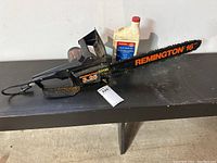 Full view of Remington electric chainsaw showing 16 inch bar, black body, orange branding, and included chain oil bottle.
