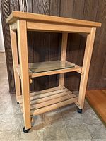 Front and side view of wooden rolling cart showing top and two lower shelves, caster wheels, and glass shelf on middle supports.