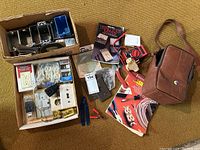 Photo of various electrical tools, hardware parts, covers, outlets, how-to books, and a brown carrying case arranged on a carpet.