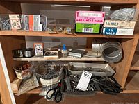 Full lot on wooden shelving showing various boxes of nails, screws, metal wire, clamps, scissors, and other hardware items.