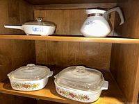 Shelf with four vintage CorningWare pieces including sauce pot, skillet, and two casserole dishes.