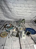 Full overview of all items including horse statue, crystal toothpick holders, scissors, spoons, postcards, letter opener, yo-yo and more arranged on white wood floor and brick backdrop