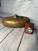 Copper and brass antique bed warming pan with removable lid, accompanied by a red vintage metal flashlight.