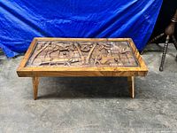 Full view of rectangular wooden coffee table with carved panel and glass top on angled legs