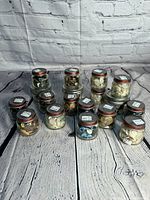 Overview of all 12 small Captain jars filled with assorted vintage buttons, arranged on wooden surface against white brick background