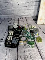 Photo showing various colorful greenish jewelry pieces arranged on a black display and wooden floor background