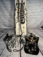 Display of numerous bead necklaces in black and gold tone bracelets arranged on a white stand and flat surface.